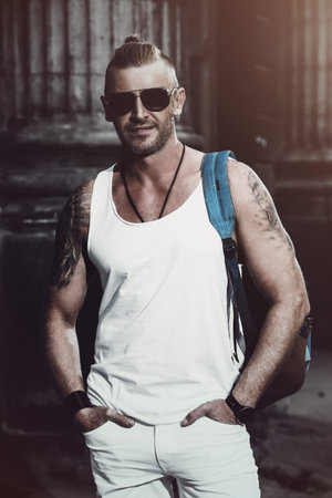 Masculine mature man with backpack standing on a city street. Sightseeing tours, travelling. Active...