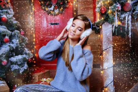 Happy girl in a warm winter clothes and earmuffs poses near the house decorated for Christmas. Time for miracles. Merry Christmas and Happy New Year.の写真素材