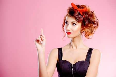 Portrait of a funny emotional young woman with curly foxy hair and a red bow on hair. Pin-up style. Bright make-up. Beauty, cosmetics.の写真素材