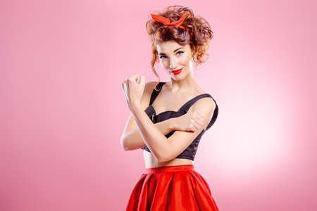 Pretty emotional young woman wearing skirt and top blouse shows indecent gesture. Pink background. Pin-up style. の写真素材