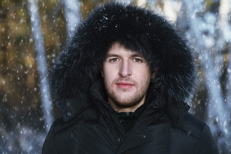 Portrait of a young man in a jacket with a hood. Man stands in winter forest.