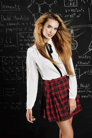 Pretty student girl with long blonde hair posing in school clothes by the chalkboard.の写真素材