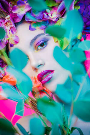 Beauty portrait. Beautiful brunette woman with sensual lilac lips surrounded by flowers. Spring look. Cosmetics, make-up. Perfumery.の写真素材