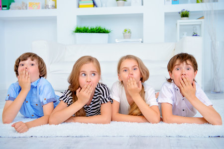 Four funny children lie on the floor at home with very surprised faces. Child concept.