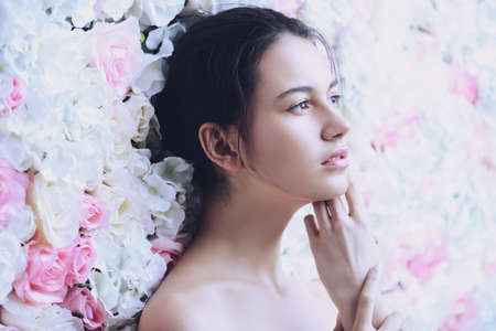 Beautiful brunette young woman with natural makeup and healthy shiny skin posing on a background of roses. Perfume, cosmetics concept.の写真素材
