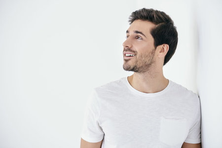 Portrait of a handsome smiling young man wearing white t-shirt. Studio shot over white background....