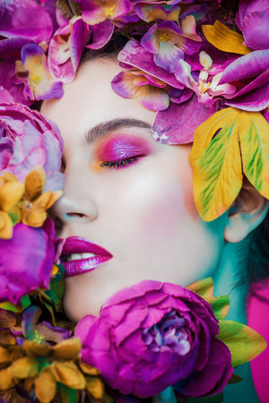 Beauty portrait. Beautiful brunette woman with sensual lilac lips surrounded by flowers. Spring look. Cosmetics, make-up. Perfumery.の写真素材