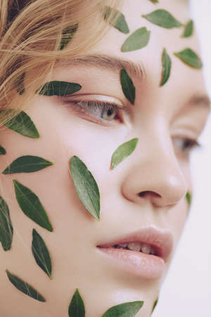 Beautiful young woman with green leaves on her face over white background. Cosmetics and makeup.の写真素材