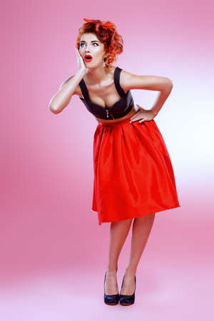 Beautiful emotional young woman wearing skirt and top blouse poses over pink background. Pin-up style. Fashion studio shot. Full length portrait. の写真素材
