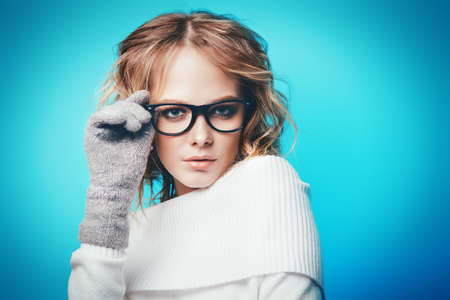 Pretty young woman posing in studio over blue background. Winter fashion concept. Youth style. Optics, eyewear.の写真素材