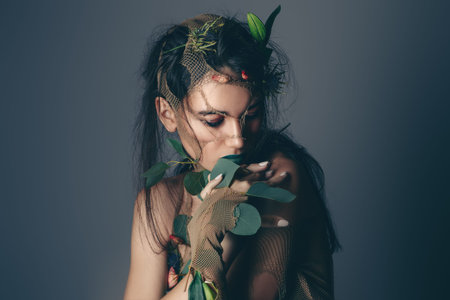 Spring Fantasy. Young woman looks like a beautiful forest nymph with green leaves and bright makeup. Cosmetics and make-up concept.の写真素材