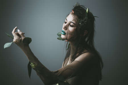 Spring Fantasy. Young woman looks like a beautiful forest nymph with green leaves and bright makeup. Cosmetics and make-up concept.の写真素材