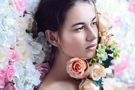 Beautiful brunette young woman with natural makeup and healthy shiny skin posing on a background of roses. Perfume, cosmetics concept.の写真素材