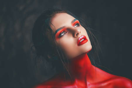 Fashion and make-up concept. Close-up portrait of an attractive young woman with creative makeup and body painting. Dark background.の写真素材
