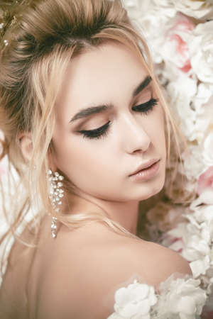 Close-up portrait of a beautiful bride woman posing by background of roses. Wedding make-up and hairstyle. Jewellery.の写真素材