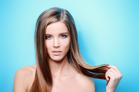 Beauty skin and hair concept. Portrait of a beautiful young woman with healthy shiny skin and hair over blue background.の写真素材