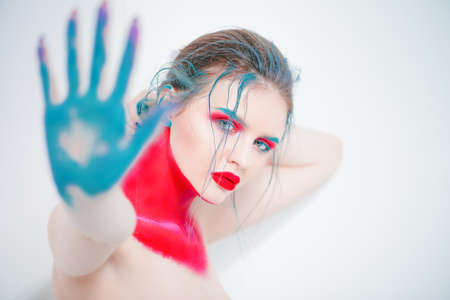 Fashion and make-up concept. Close-up portrait of an attractive young woman with creative makeup and body painting. Red background.の写真素材