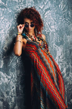 Beautiful bright woman with curly foxy hair wears a dress and beads in boho style. Ethnic style in clothes.の写真素材
