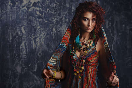 Portrait of a beautiful red-haired woman wears a kerchief, earrings and beads in boho style. Ethnic style in accessories.の写真素材
