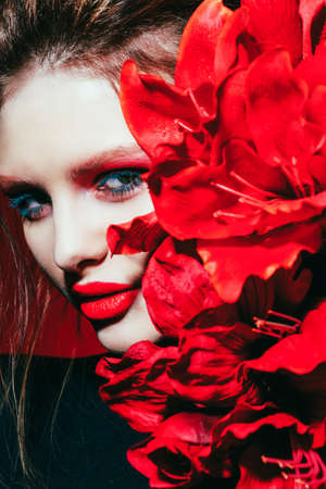Fashion and make-up concept. Close-up portrait of an attractive young woman with creative makeup and red flower.の写真素材