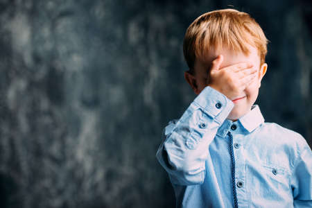 Five year old boy covered his eyes with his hand. Childhood. Children's games.の写真素材