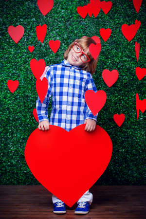 Ð¡ute child boy holding big heart surrounded by little hearts over lawny background. First love. Valentine's Day. の写真素材