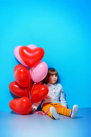 ?ute six-year-old boy holding heart shaped balloons over blue background. Valentine's Day. の写真素材