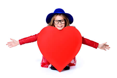 Funny child girl sits behind a big heart with her arms outstretched. Isolated over white. First love. Valentine's Day. の写真素材