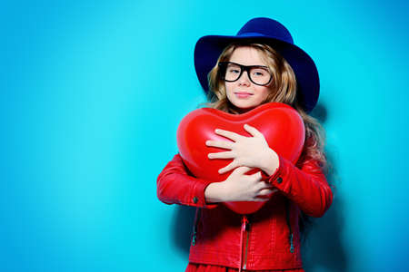 Pretty ten-year-old girl holding heart shaped balloon over blue background. First love. Valentine's Day. の写真素材