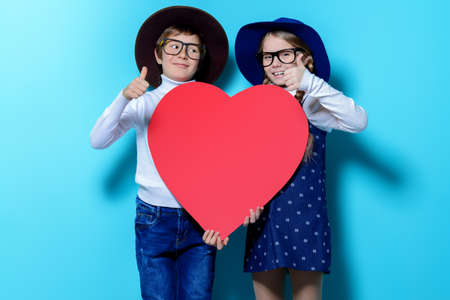 Happy pre-teen boy and girl holding big red heart over blue background. Friendship. First love. Valentine's Day. の写真素材