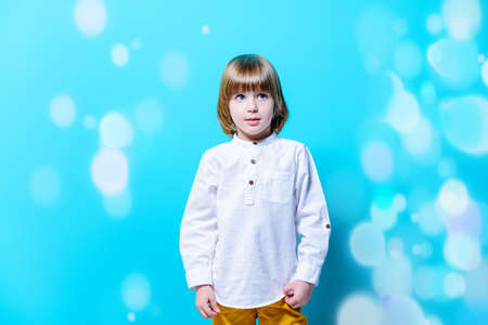Ð¡ute six-year-old boy poses holding over blue background. Children's fashion. Studio shot.の写真素材