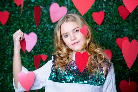 Happy pre-teen girl poses surrounded by little hearts over lawny background. First love. Valentine's Day.の写真素材
