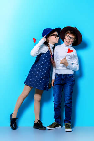 Happy pre-teen boy and girl holding two little hearts over blue background. Friendship. First love. Valentine's Day. の写真素材
