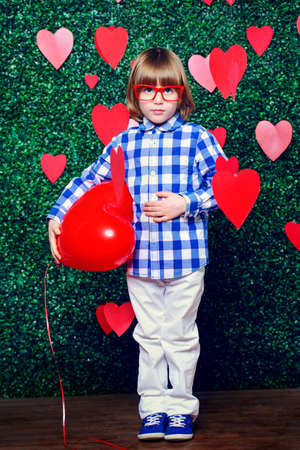 Ð¡ute child boy holding heart shaped balloon, surrounded by hearts over lawny background. First love. Valentine's Day. の写真素材