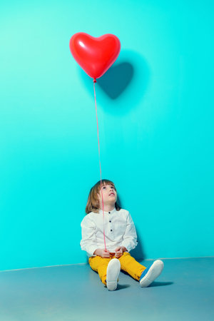 Ð¡ute six-year-old boy holding heart shaped balloon over blue background. Valentine's Day. の写真素材