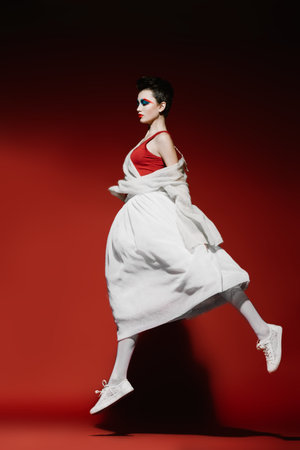 Beautiful female model in stylish clothes jumping over red background. Beauty, fashion. Studio shot.