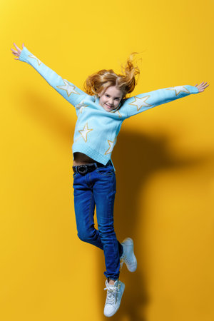 Joyful pre-teen girl jumping over yellow background. Full length studio shot. Happiness, activity...