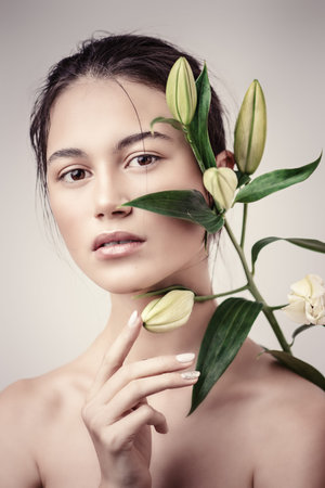 Beauty portrait. Sensual brunette girl with a green spring plant. Beauty, natural cosmetics concept.の写真素材