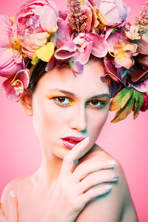Sensual spring lady in a wreath of flowers over pink background. Inspiration of spring and summer. Perfume, cosmetics concept.の写真素材