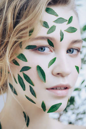 Beautiful young woman with green leaves on her face over white background. Cosmetics and makeup.の写真素材