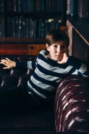 Modern boy in elegant clothes sitting on a sofa in luxurious apartments. School fashion. の写真素材