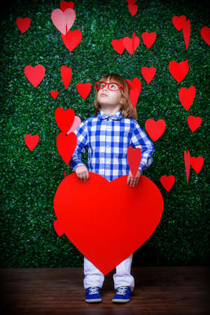 Ð¡ute child boy holding big heart surrounded by little hearts over lawny background. First love. Valentine's Day. の写真素材