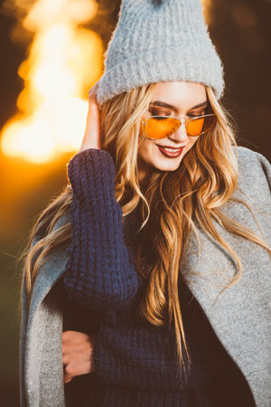 Happy young woman wearing warm sweater, a coat and a woolen hat walking in the park at a sunny...