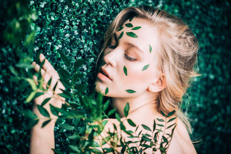 Beautiful young woman with green leaves on her face over green background. Cosmetics and makeup.の写真素材
