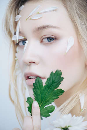 Beautiful young woman with petals of chrysanthemum on face. Beauty, natural cosmetics concept.の写真素材