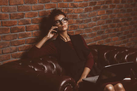 Elegant businesswoman is working on a laptop at the office and talking on her cell phone. Contemporary business.の写真素材