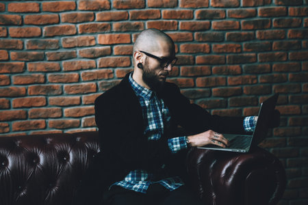 Young brutal businessman is working at home using his laptop. Male beauty, fashion. Business...