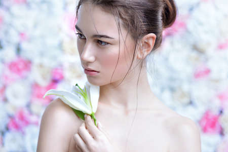 Beautiful brunette young woman with natural makeup and healthy shiny skin posing on a background of roses. Perfume, cosmetics concept.の写真素材