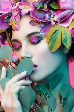 Beauty portrait. Beautiful brunette woman with sensual lilac lips surrounded by flowers. Spring look. Cosmetics, make-up. Perfumery.の写真素材