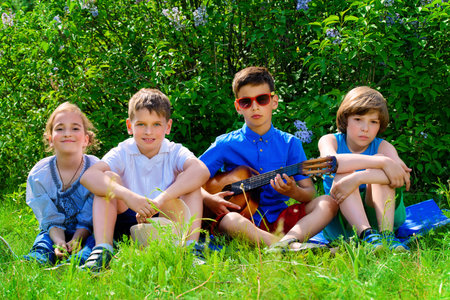 Group of cheerful children resting in the park with songs and guitar. Outdoor activity. Summer...